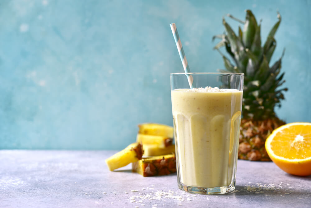 Pina colada ve sklenici s brčkem proti modrému pozadí s ananasem